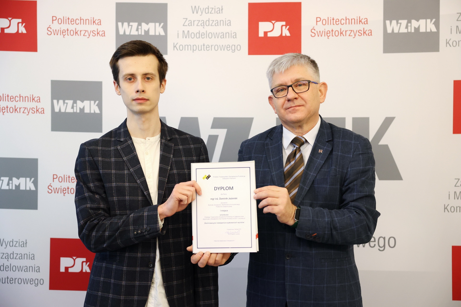 Dwóch mężczyzn trzyma dyplom. W tle logo Politechniki Świętokrzyskiej.