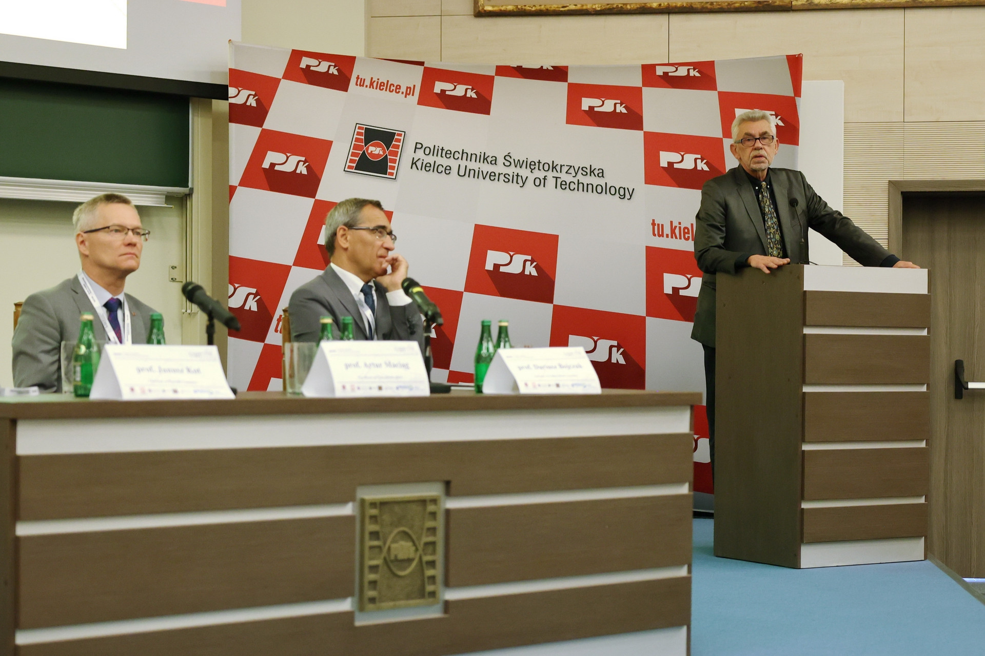 Trzech mężczyzn w garniturach, jeden przemawia przy mównicy. Konferencja Politechniki Świętokrzyskiej.