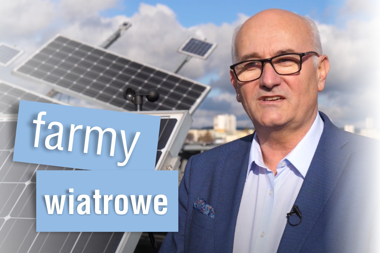 Mężczyzna w okularach stoi na tle farm wiatrowych i paneli słonecznych. Kontekst: energia odnawialna.